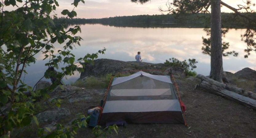 a person sits near the shore of their campsite. 